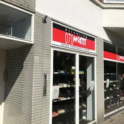 Winkelpui van 070watt kringloopwinkel met rode en zwarte letters op gevel, glazen deuren en ramen met uitzicht op winkelinter