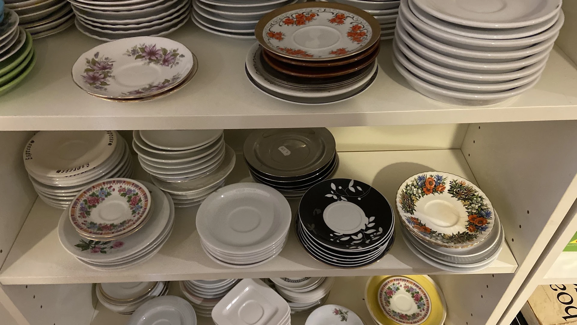 Schappen met verzameling serviesgoed: borden, schotels en kopjes in verschillende stijlen en kleuren
