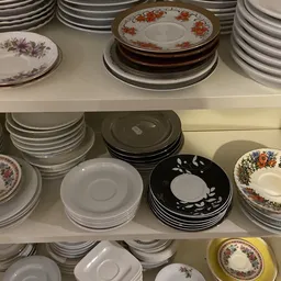 Schappen met verzameling serviesgoed: borden, schotels en kopjes in verschillende stijlen en kleuren