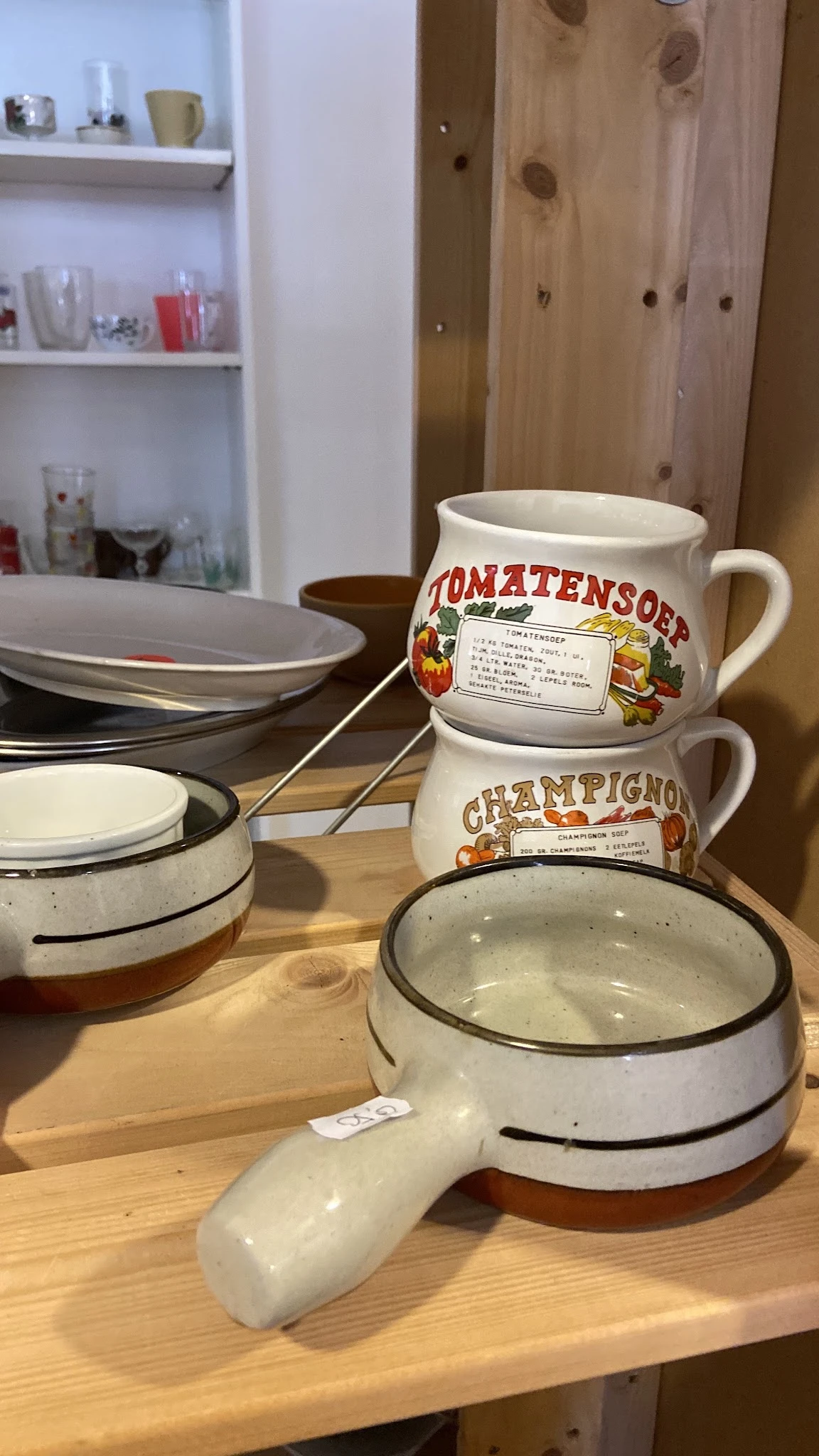 Vintage emaille pannen en mokken met opdruk, gestapeld op houten tafel