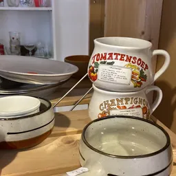 Vintage emaille pannen en mokken met opdruk, gestapeld op houten tafel