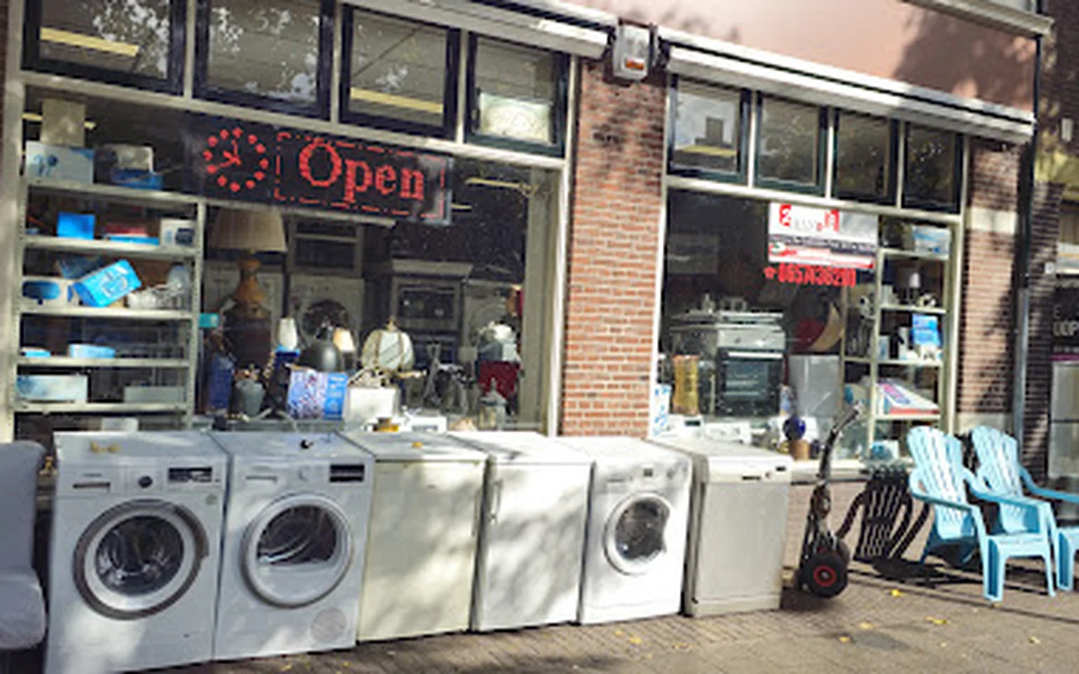 Voorgevel van kringloopwinkel met wasmachiines en drogers uitgestald voor het raam, neonreclame 'Open' zichtbaar