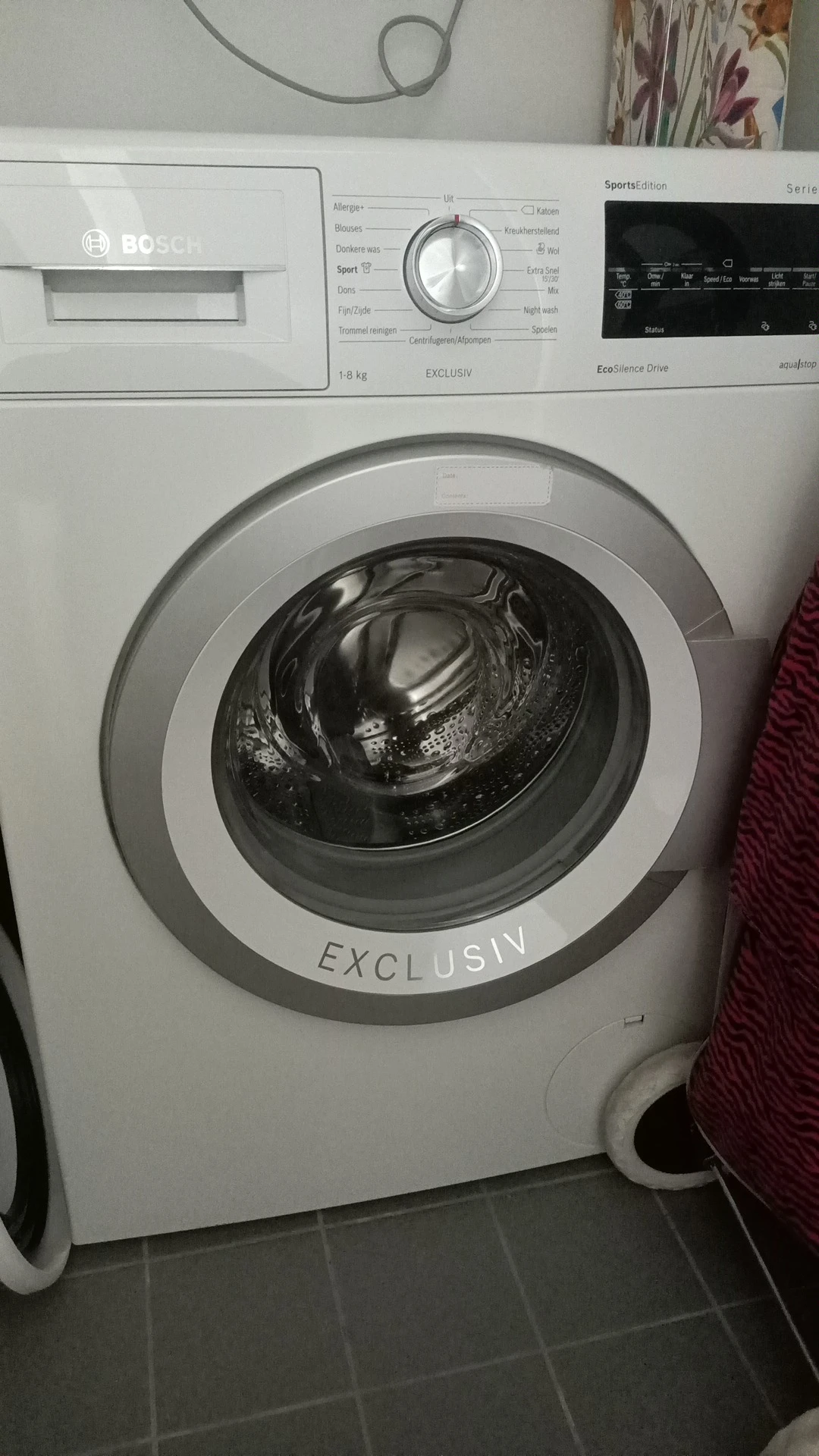 Close-up van een witte wasmachine met 'EXCLUSIV' op de behuizing, deur open met trommel zichtbaar