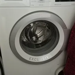 Close-up van een witte wasmachine met 'EXCLUSIV' op de behuizing, deur open met trommel zichtbaar