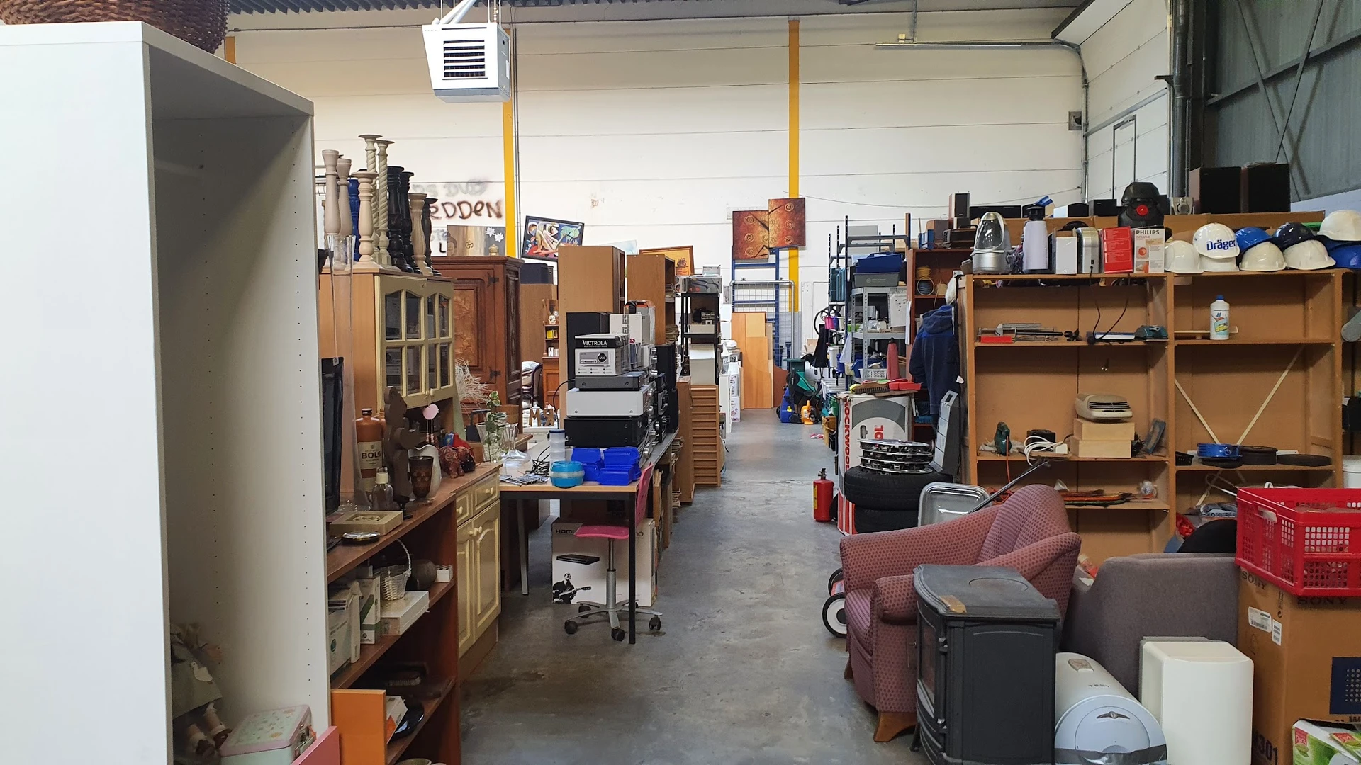 Overzicht van de winkelvloer met houten meubels, stellingen, dozen en diverse tweedehands spullen