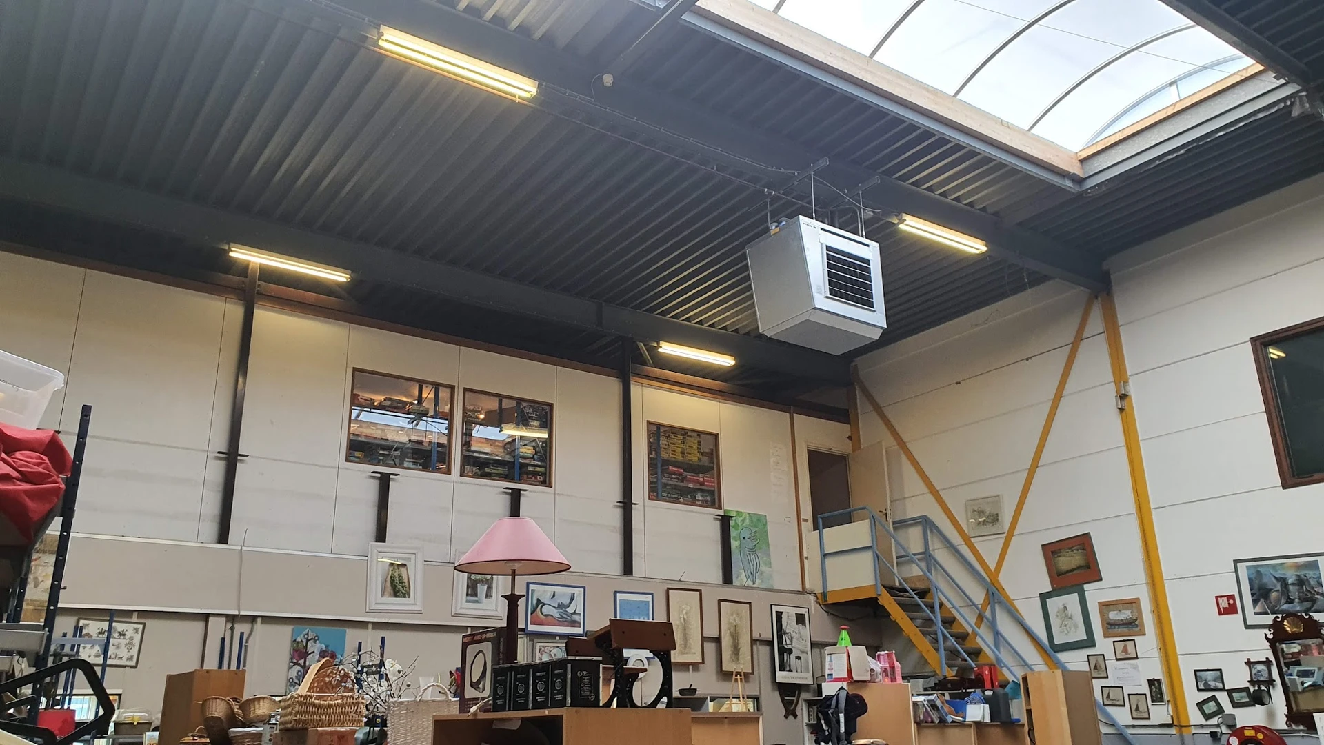 Interieur van kringloopwinkel met stellingen, kunstwerken aan muren en diverse tweedehandsartikelen op toonbank