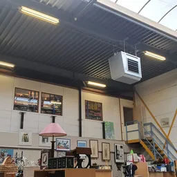Interieur van kringloopwinkel met stellingen, kunstwerken aan muren en diverse tweedehandsartikelen op toonbank
