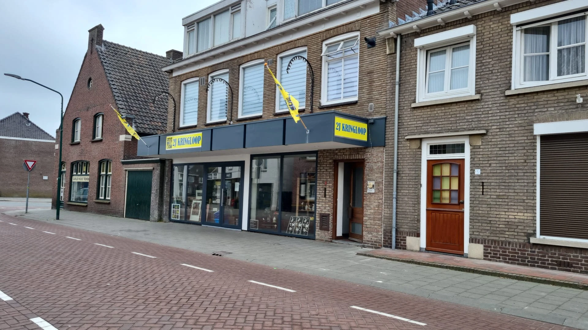 Voorgevel van kringloopwinkel met blauwe gevel, ramen, groene deur links en rode deur rechts aan Emmerikstraat