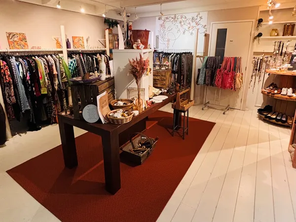 Overzicht van winkelinterieur met kledingrekken, een centraal houten display-tafel met accessoires en decoratie, rode loper, 