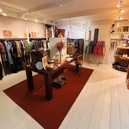 Winkelvloer van kringloopwinkel met kledingrekken, centrale display met decoratie en rode vloermat