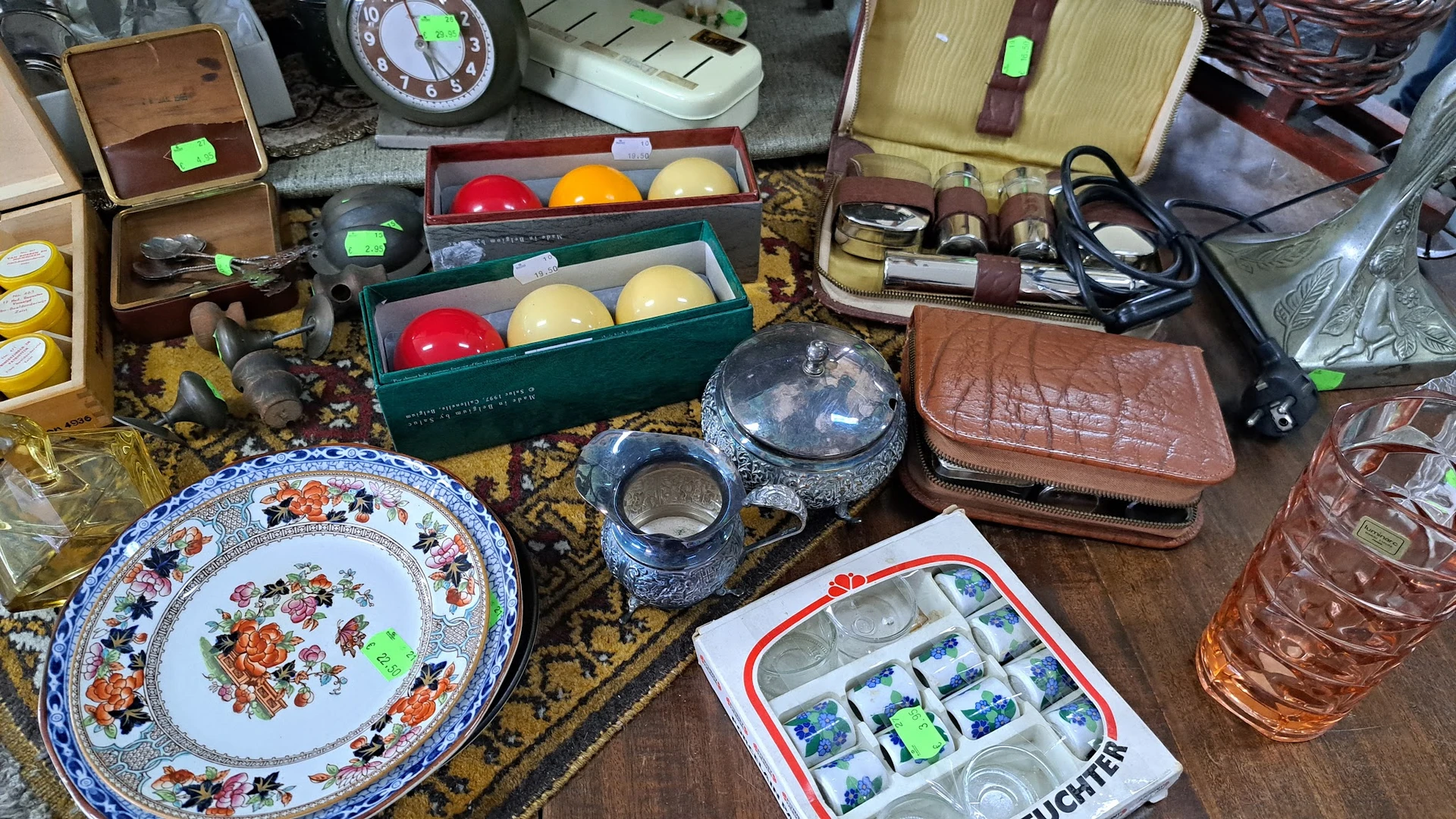 Diverse tweedehandsartikelen op een tafel: biljartballen, servies, portemonnees, sieraden en huishoudelijke spullen