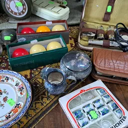Diverse tweedehandsartikelen op een tafel: biljartballen, servies, portemonnees, sieraden en huishoudelijke spullen