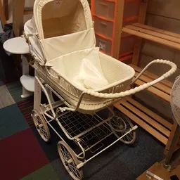 Vintage kinderwagen in crème-wit met zwart metalen onderstel, open verkocht in kringloopwinkel