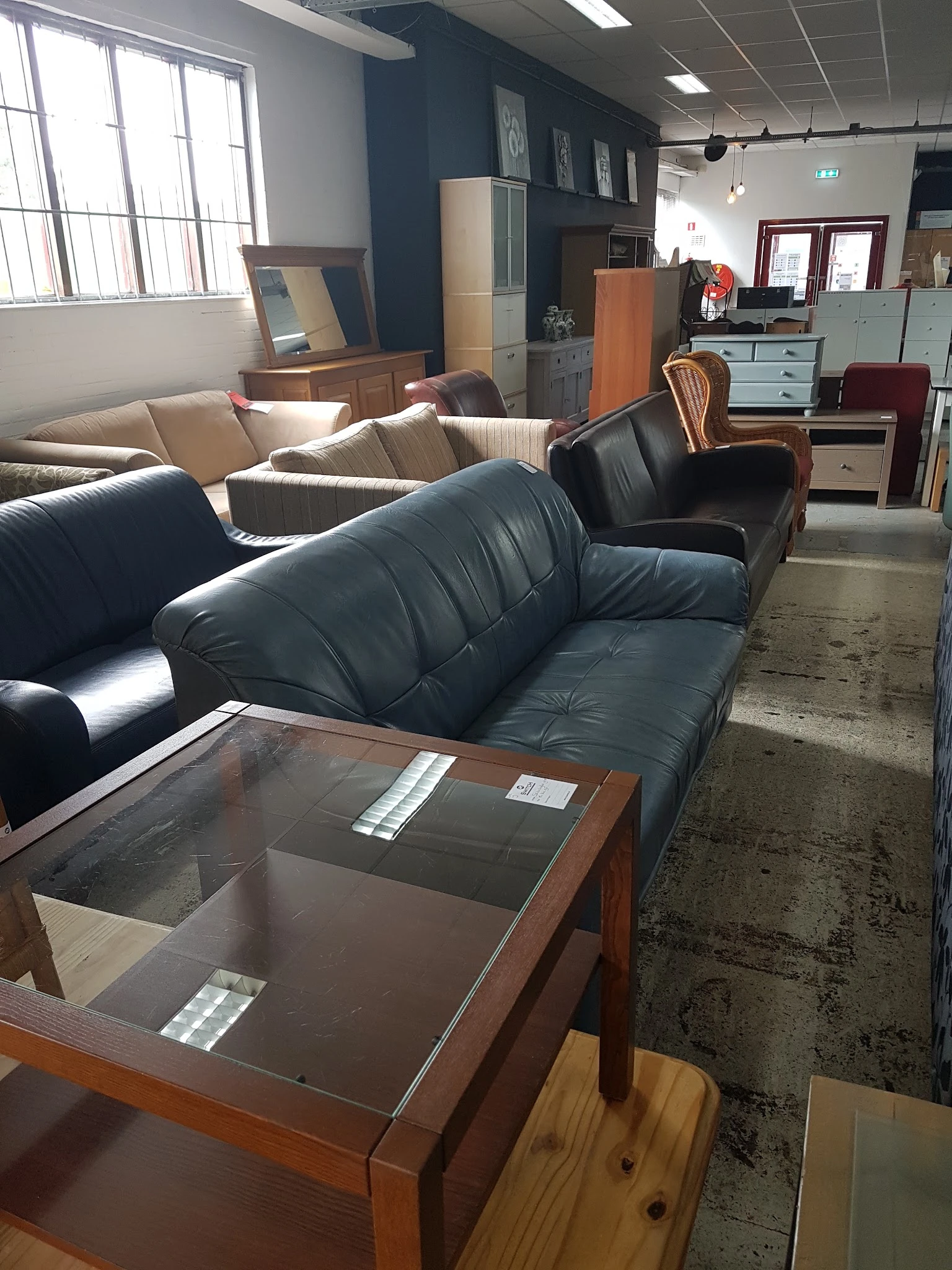 Uitgestalde zwarte leren banken en fauteuils in de kringloopwinkel met houten salontafel