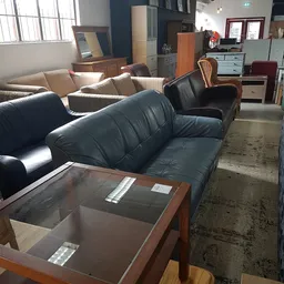 Uitgestalde zwarte leren banken en fauteuils in de kringloopwinkel met houten salontafel