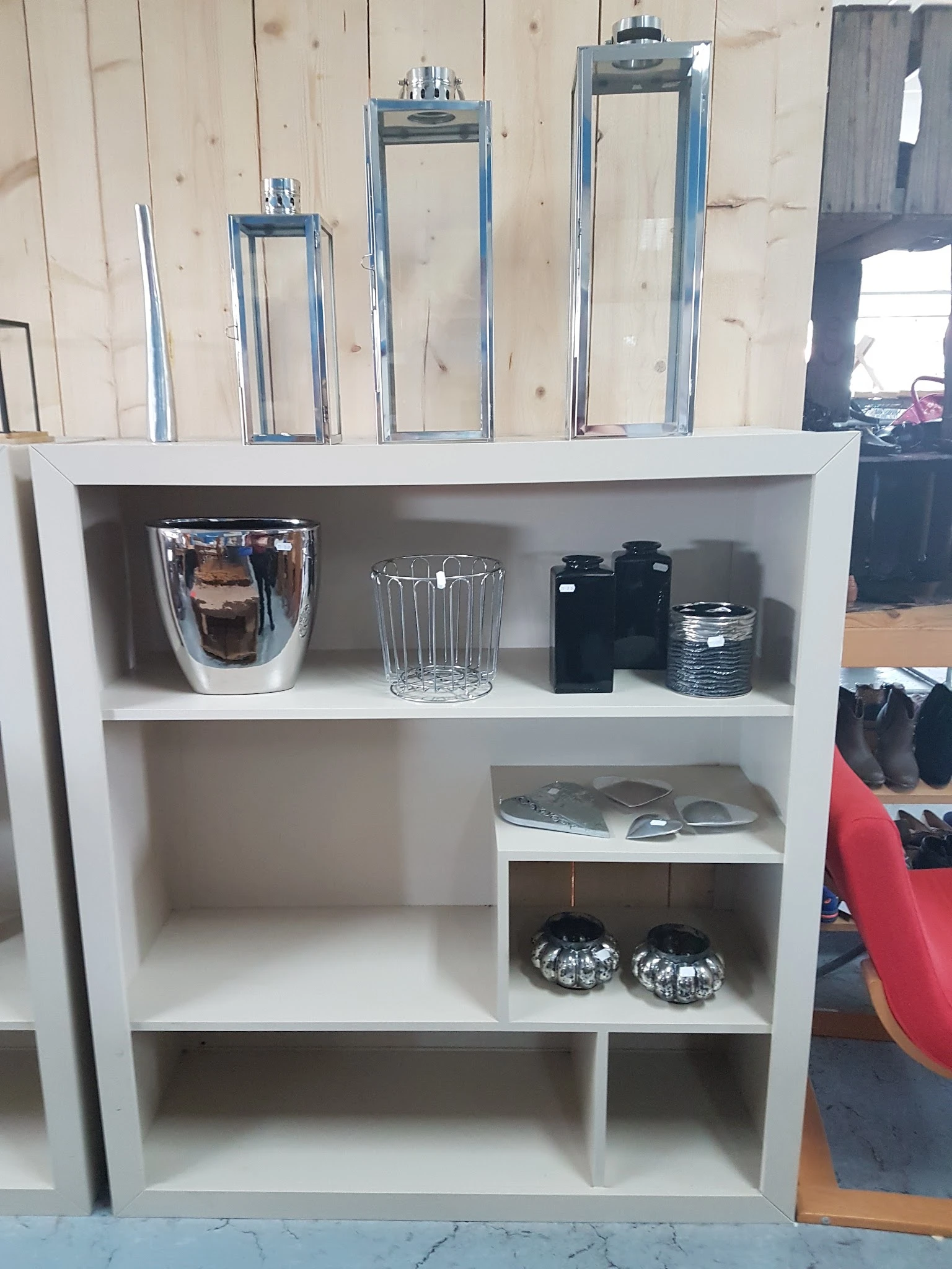 Witte boekenkast met huishoudelijke artikelen zoals een koffiezetapparaat, glazen, zwarte containers en decoratieve items.