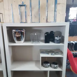 Witte boekenkast met huishoudelijke artikelen zoals een koffiezetapparaat, glazen, zwarte containers en decoratieve items.
