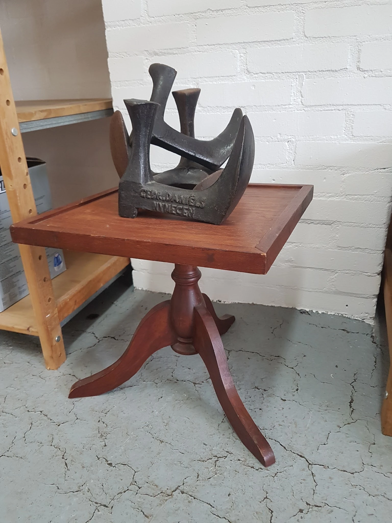 Rood houten pedestal-tafeltje met zwart sculptuur erop in een kringloopwinkel