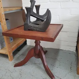 Rood houten pedestal-tafeltje met zwart sculptuur erop in een kringloopwinkel