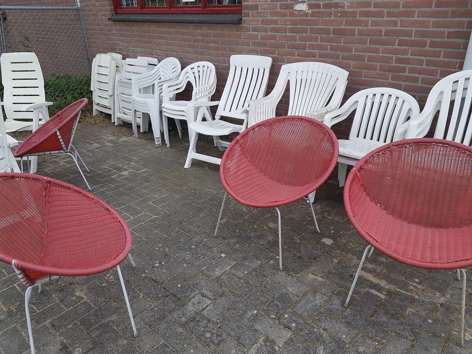 Tuinstoelen en loungestoelen in rood en wit op een terras tegen een bakstenen muur