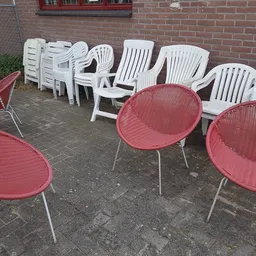 Tuinstoelen en loungestoelen in rood en wit op een terras tegen een bakstenen muur