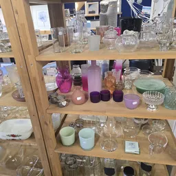 Glazen kastje met diverse glazen, kaarsen in paarse tinten en andere huishoudartikelen uitgestald