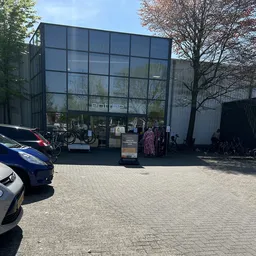 Voorgevel van kringloopwinkel met groot glasraam, winkelnaam 'entrée' zichtbaar, parkeerplaats met auto's ervoor