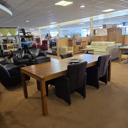 Winkelvloer met houten eettafel, zwarte stoelen en diverse meubels op de achtergrond
