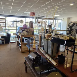 Ruime kringloopwinkel met diverse meubels, standaards en huishoudelijke artikelen uitgestald op de vloer en stellingen