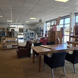 Winkelvloer met houten tafel, bruine stoelen, kasten met decoratie en meubels langs de muren in kringloopwinkel