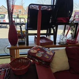 Uitgestalde tweedehands artikelen: vintage koffer, manden, vazen en ander huishoudelijk spul op een tafel bij het raam