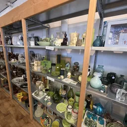 Glazen stellingkast met groen thema: flessen, vazen, decoratieve items en huishoudgoederen uitgestald