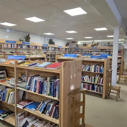 Boekenrekken met blauwe etiketten en boeken in een kringloopwinkel, houten kasten in een grote lichte zaal