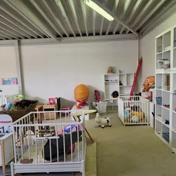 Afdeling speelgoed in kringloopwinkel met witte speelgoedkeukens, witte stellingen, groen vloerkleed en diverse speelgoedarti