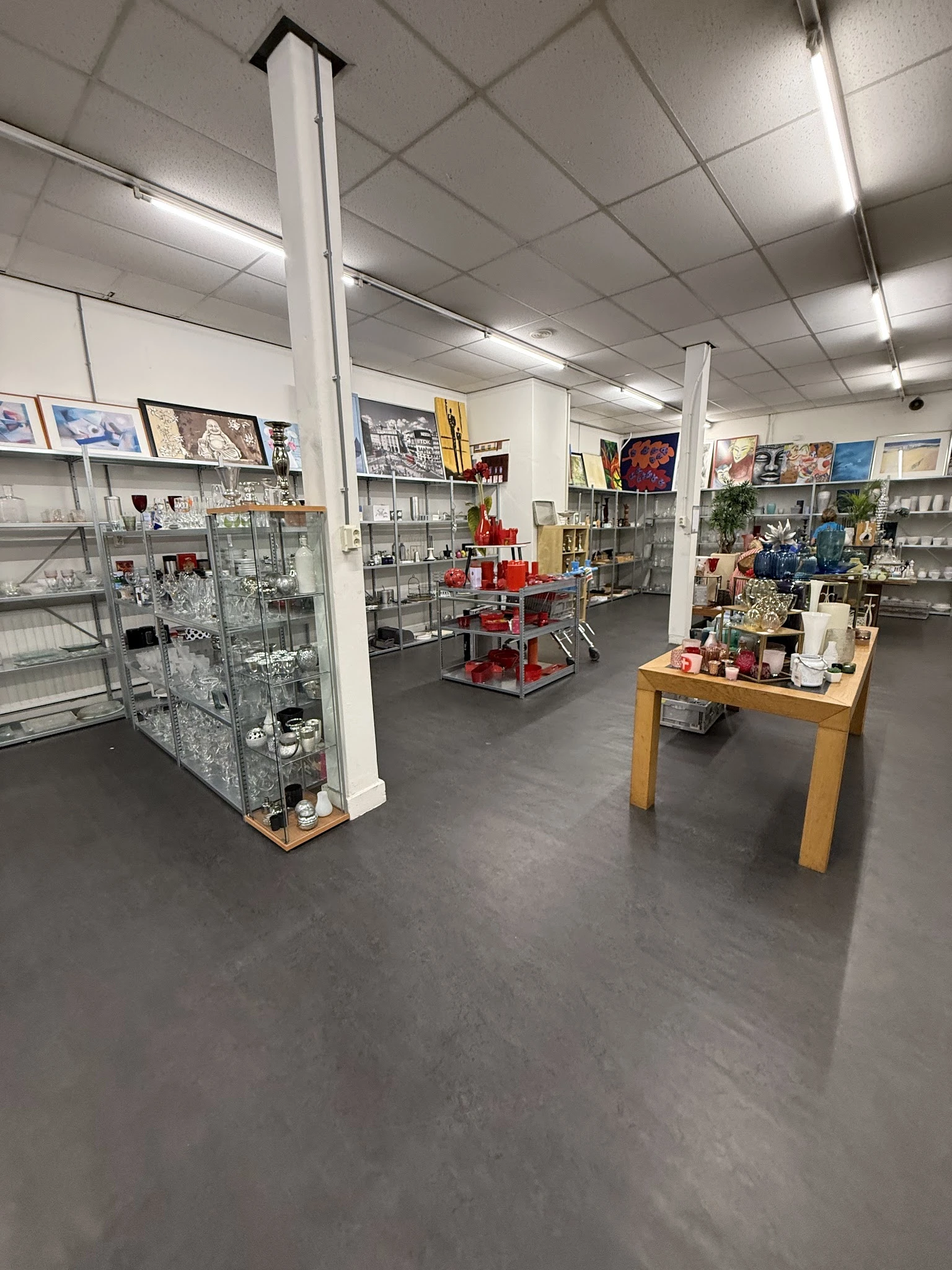 Overzicht van kringloopwinkel met glazen vitrinekasten, stellingen en houten tafel met merchandise
