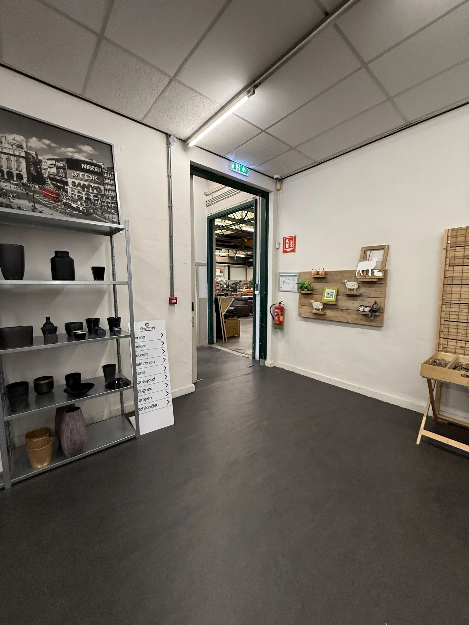 Winkelvloer met stellingen met zwarte huishoudspullen, houten wandpanelen met decoratieve artikelen, en zicht op deuropening 