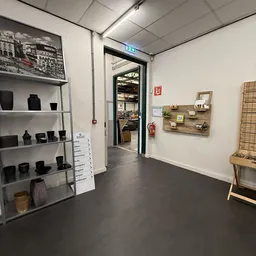 Winkelvloer met stellingen met zwarte huishoudspullen, houten wandpanelen met decoratieve artikelen, en zicht op deuropening 
