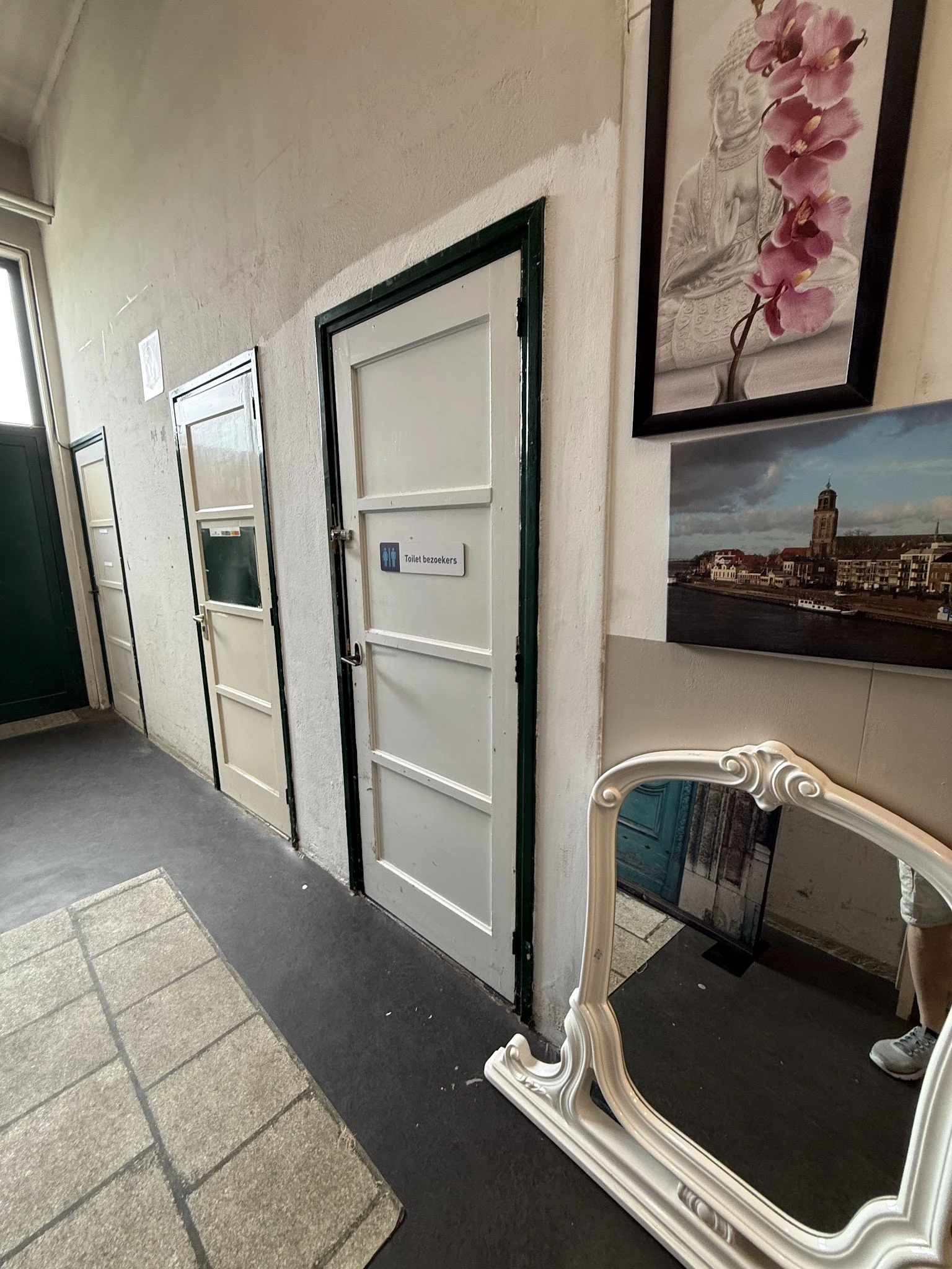 Hal met witte deuren, enkele muurfoto's en een decoratieve spiegel in een kringloopwinkel