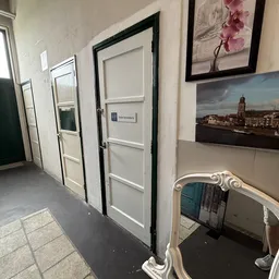 Hal met witte deuren, enkele muurfoto's en een decoratieve spiegel in een kringloopwinkel
