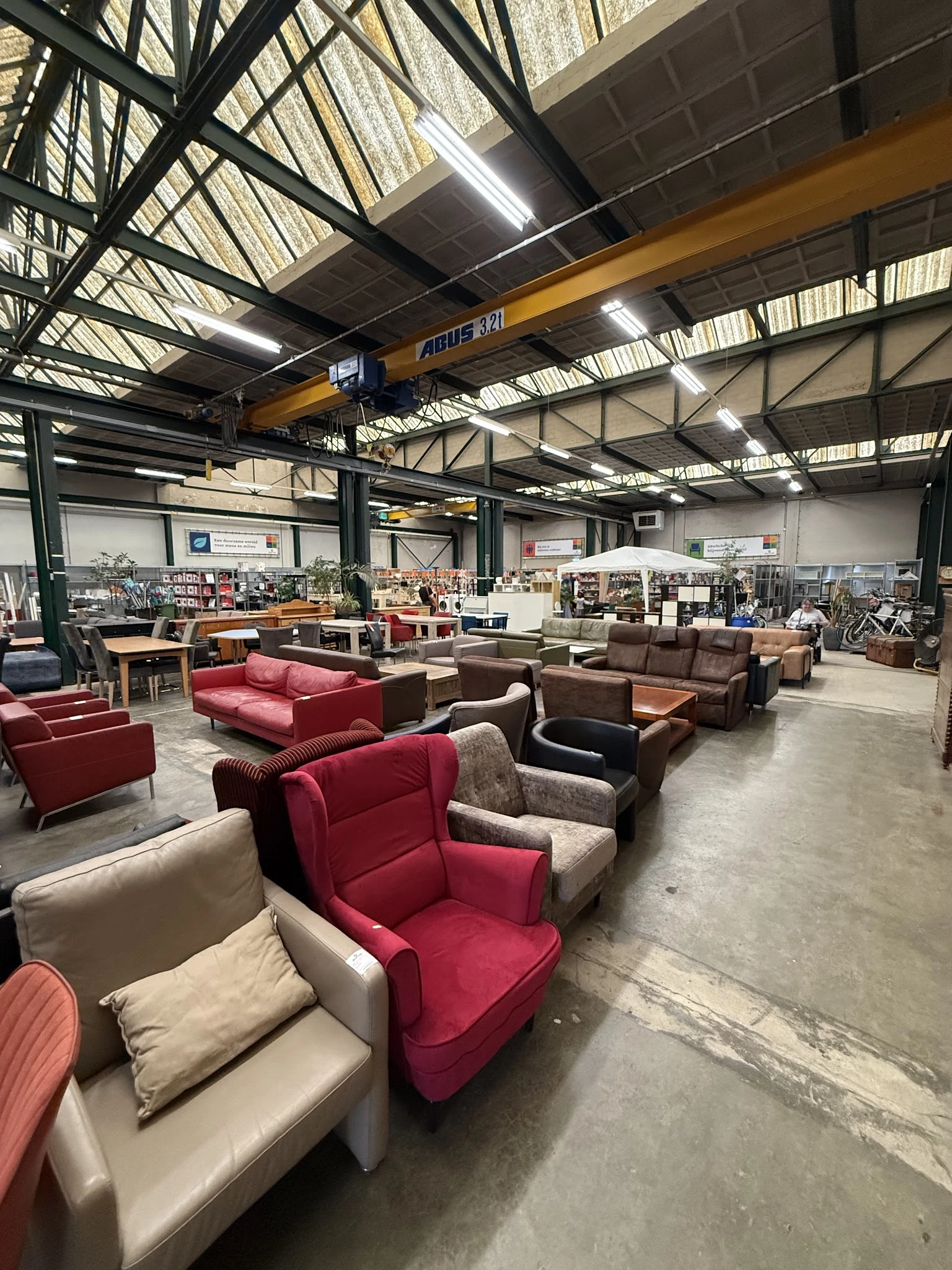Ruim magazijn met verschillende tweedehands meubels zoals fauteuils, zetels en banken in rood, bruin en beige