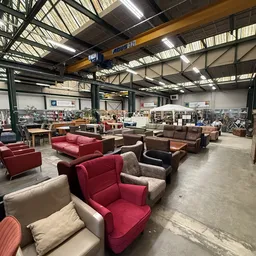 Ruim magazijn met verschillende tweedehands meubels zoals fauteuils, zetels en banken in rood, bruin en beige