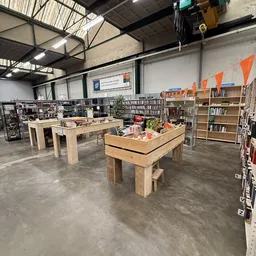 Winkelvloer met houten tafels, boekenkasten, stellingen en diverse tweedehands spullen in een ruime hal met industrieel plafo