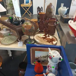 Uitgestalde tweedehandsartikelen op tafel: wereldbol, houten beelden, servies, decoratieve items en kunststofvoorwerpen