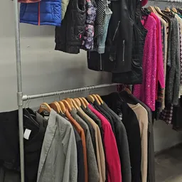 Rekken met tweedehands dameskleding op houten hangers, waaronder jassen, truien en jurken in verschillende kleuren