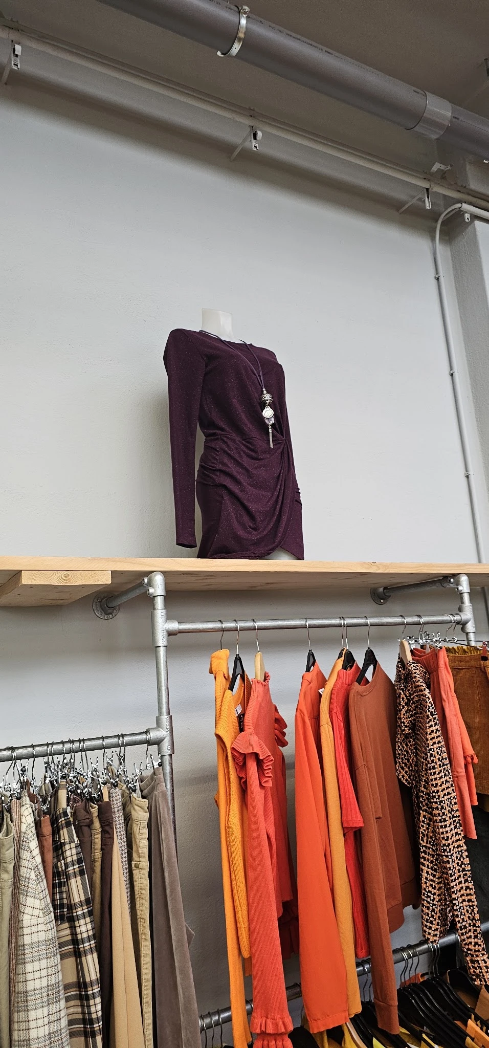 Houten wandplank met paarse top en daaronder een stang met hangers met oranje en bruine kledingstukken