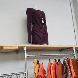 Houten wandplank met paarse top en daaronder een stang met hangers met oranje en bruine kledingstukken