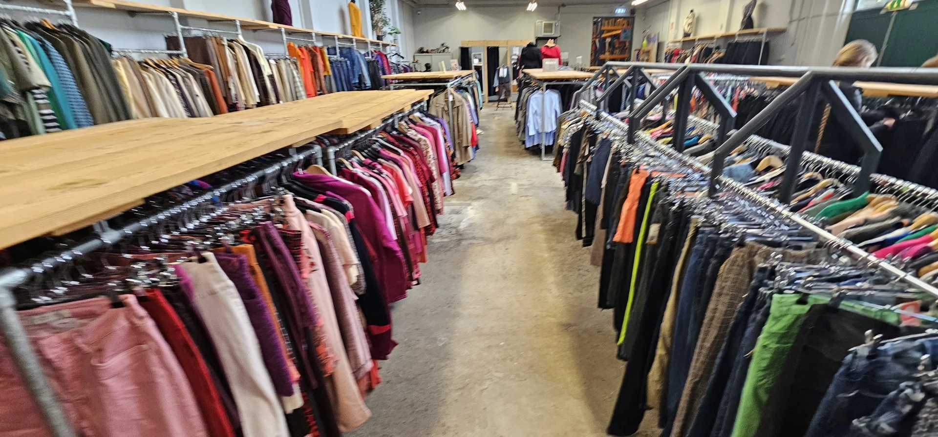 Rekken met tweedehands dameskleding in verschillende kleuren, gerangschikt op kleerhanger in een kringloopwinkel