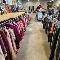 Rekken met tweedehands dameskleding in verschillende kleuren, gerangschikt op kleerhanger in een kringloopwinkel