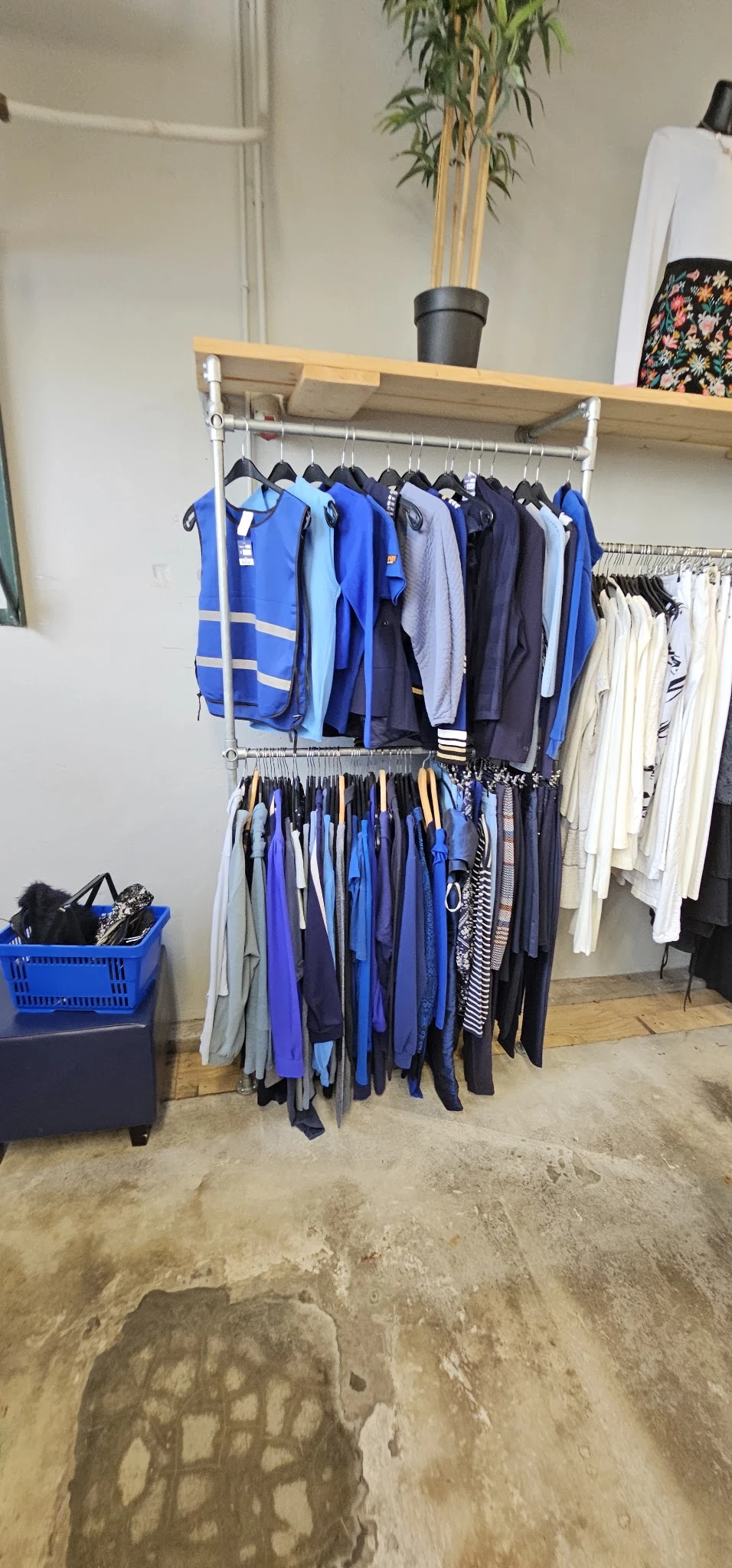 Rekken met tweedehands kleding in verschillende kleuren, vooral blauwe en donkere tinten