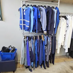 Rekken met tweedehands kleding in verschillende kleuren, vooral blauwe en donkere tinten